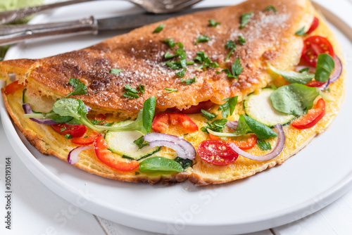 Omelette with zucchini, lamb's lettuce, tomatoes and red pepper on plate. Frittata - italian omelet.