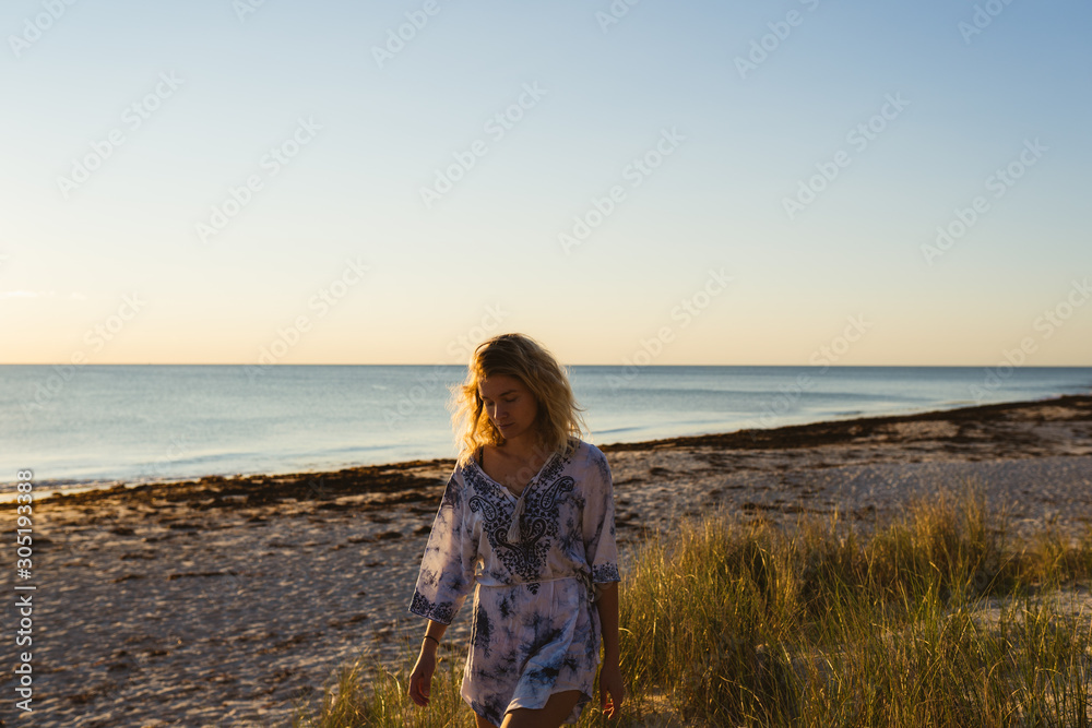 Young woman with blonde hair on an evening walk at sunset on the beach exploring the sand dunes and enjoying the summer evening at Cottesloe beach, Perth, Western Australia.