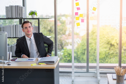 Handsome businessman relaxing during working in office with desktop computer and documents on desk. Professional business background and work life balance concept.