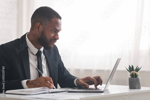 Foto Concentrated business clerk making notes, using laptop