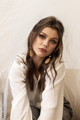 Beautiful young curly brunette girl in white blouse and grey pants