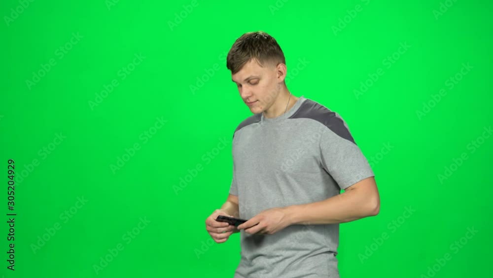 Smiling man goes and texting with smartphone on green screen at studio.