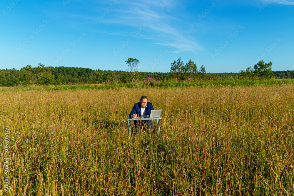 White caucasian man with a beard works at table on a laptop outdoors. Concept businessman outdoors. White caucasian man with a beard works at table on a laptop outdoors. Concept businessman outdoors.