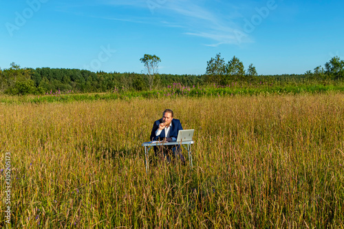 White caucasian man with a beard works at table on a laptop outdoors. Concept businessman outdoors.