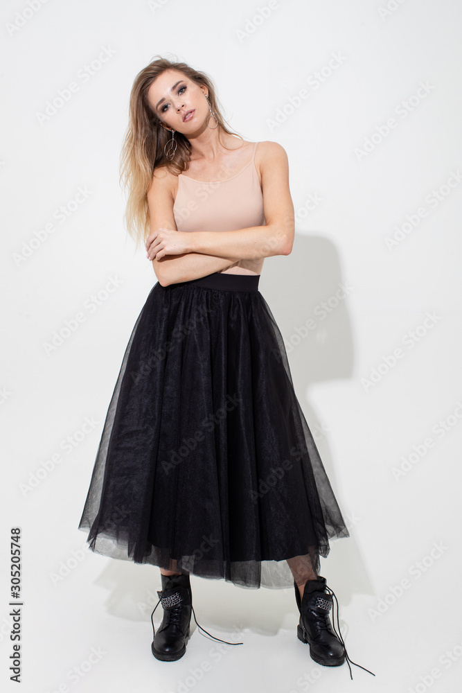 Beautiful girl in a light t-shirt and black skirt posing on a white background. Fashion shooting