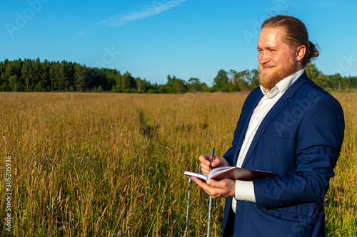 A white caucasian man with a beard is writing in a notebook outdoors. Concept businessman outdoors.
