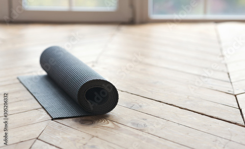 Rolled up fitness mat on wooden floor at yoga studio