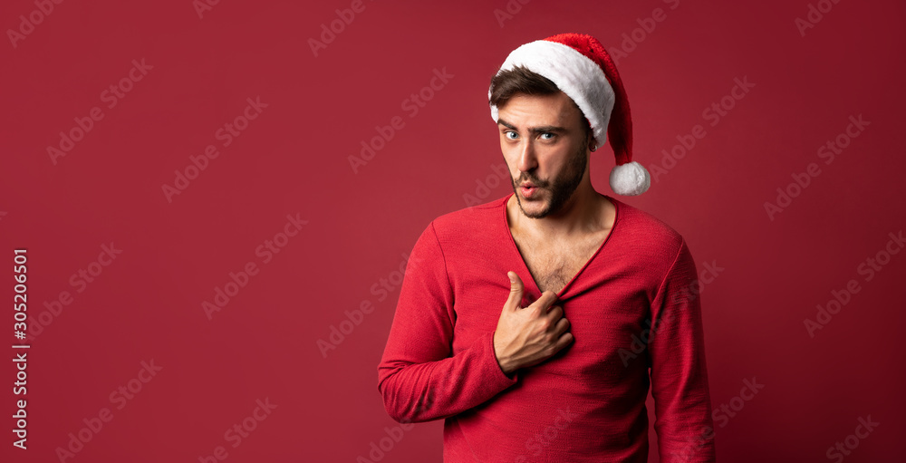 Young handsome caucasian guy in red sweater and Santa hats stands on red background in studio and Shows how hot he is Young handsome caucasian guy in red sweater and Santa hats stands on red background in studio and Shows how hot he is