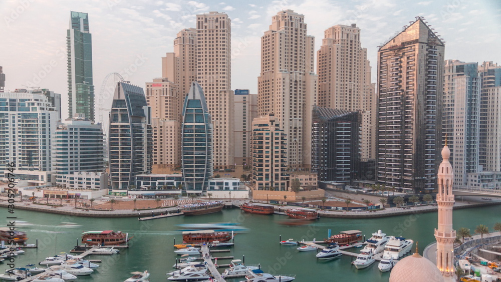 Fototapeta premium Yachts in Dubai Marina flanked by the Al Rahim Mosque and residential towers and skyscrapers aerial timelapse.
