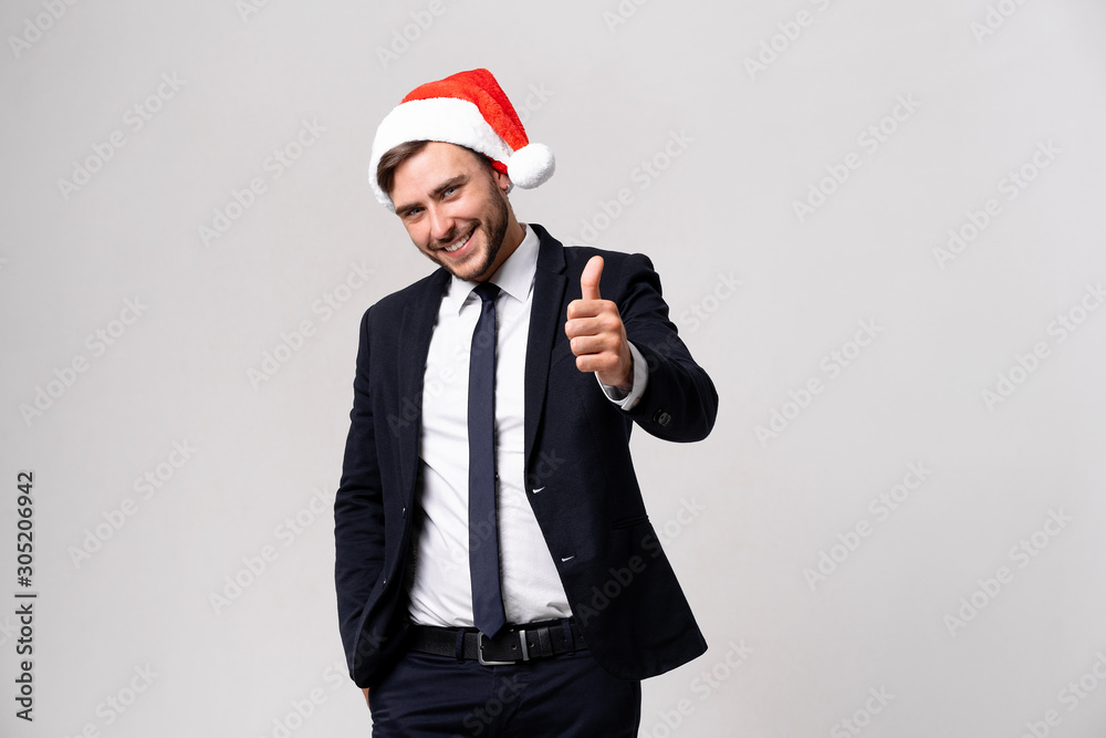 Young handsome caucasian guy in business suit and Santa hats stands on white background in studio smilie and showing thumbs up. Young handsome caucasian guy in business suit and Santa hats stands on white background in studio smilie and showing thumbs up.
