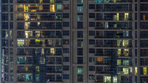 Rows of glowing windows with people in apartment building at night. © neiezhmakov