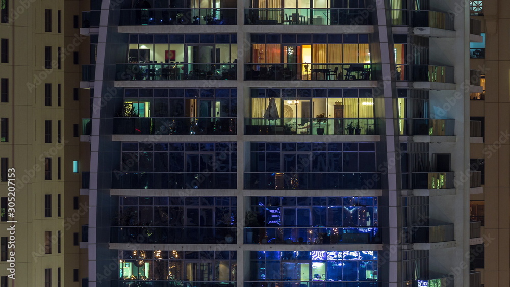 Rows of glowing windows with people in apartment building at night.