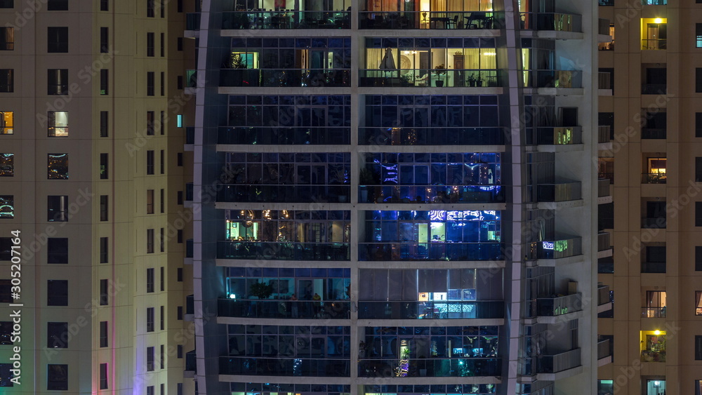 Rows of glowing windows with people in apartment building at night.