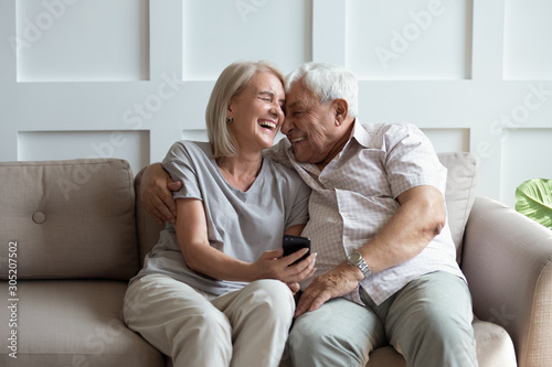 Overjoyed mature family spouse watching funny photos on mobile phone.