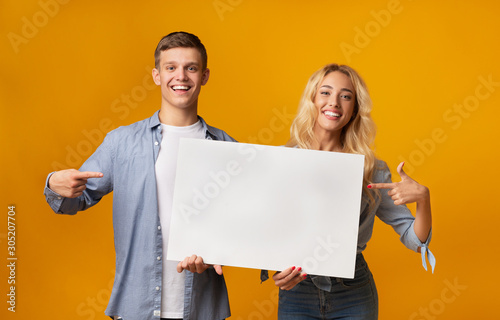 Young couple holding blank advertising board and pointing on it photo