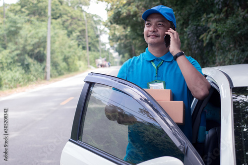 Cheerful asian delivery man holding a box and smiling while standing on road background