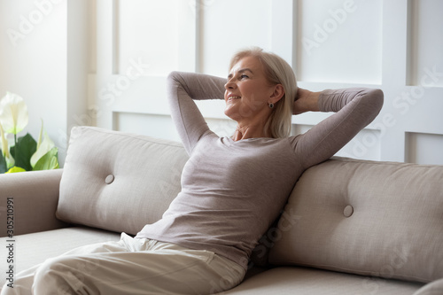 Happy middle aged retired woman relaxing on comfortable sofa.