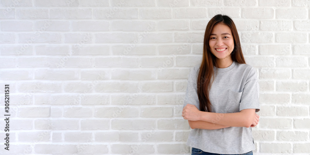 Portrait of young asian woman standing and smiling over white brick wall background, Happy asia girl smiling and looking at camera in casual lifestyle Portrait of young asian woman standing and smiling over white brick wall background, Happy asia girl smiling and looking at camera in casual lifestyle