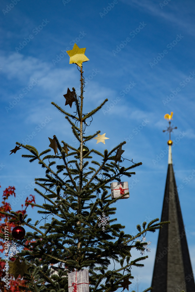 festlich dekorierter Weihnachtsbaum vor einem dörflichen Kirchturm, blauer Himmer festlich dekorierter Weihnachtsbaum vor einem dörflichen Kirchturm, blauer Himmer