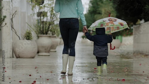 Mom with her son are walking in the rain in rubber boots and umbrellas.