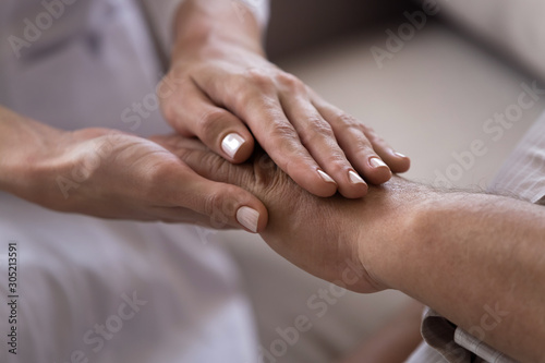 Close up young female medical worker holding hand of old male patient.