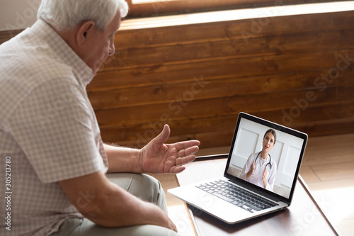 Focused older 80s patient consulting with doctor via video call. photo