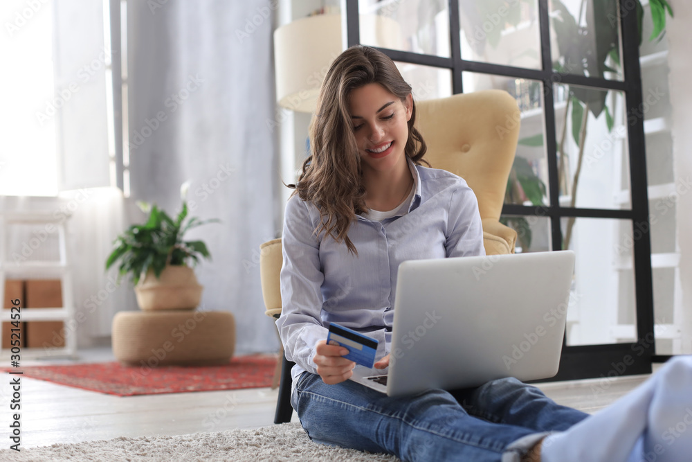 Happy natural brunette using credit card and laptop in the living room. Happy natural brunette using credit card and laptop in the living room.