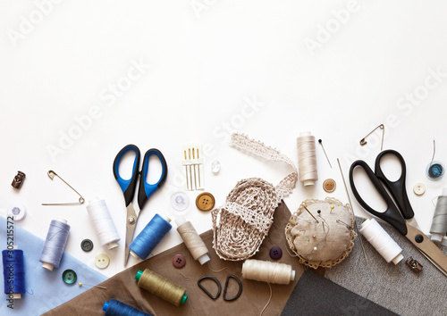 Flat lay composition with sewing accessories: threads, fabrics, scissors, buttons, needles, pins and other sewing tools on a white background. Top view, copy space, mock up. photo