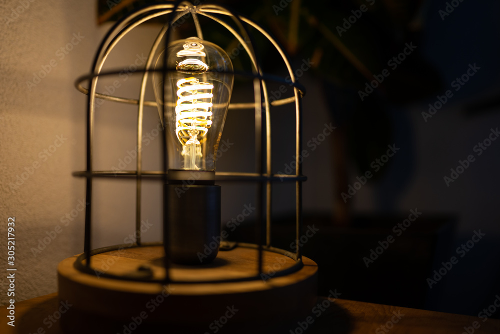 A caged filament light bulb with shadow play on the wall. In a home with a warm and cozy mood ambiance during winter.