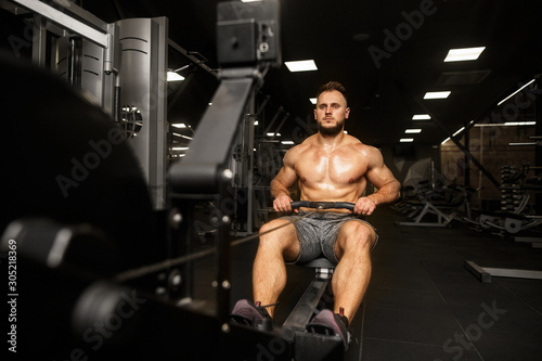 Man working out on row machine in dark gym at night. ROWING SPORT.