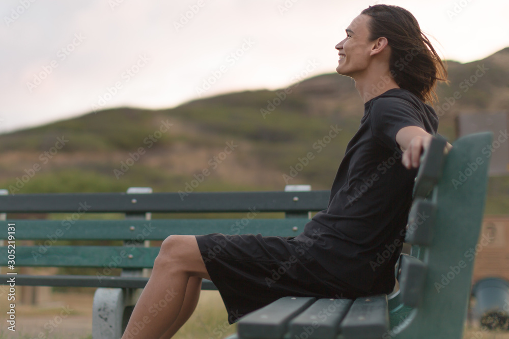 Happy young man sitting on a bench outside, feeling good.