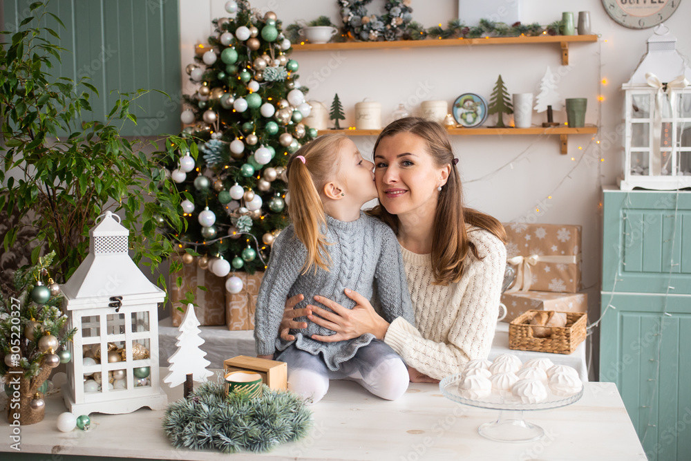 Girl kissing her mother while sitting on kitchen table in Christmas at home.
