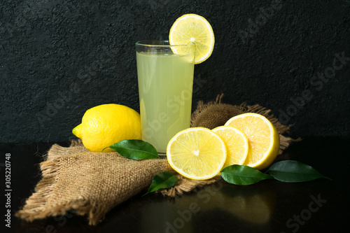 Glass of lemon juice and lemons on a black background. Vitamin drink.