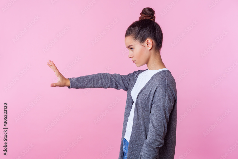 Stop! Side view of strict teenage girl with bun hairstyle in casual clothes standing with raised hand showing prohibition ban block gesture with palm, negative expression. studio shot, pink background Stop! Side view of strict teenage girl with bun hairstyle in casual clothes standing with raised hand showing prohibition ban block gesture with palm, negative expression. studio shot, pink background