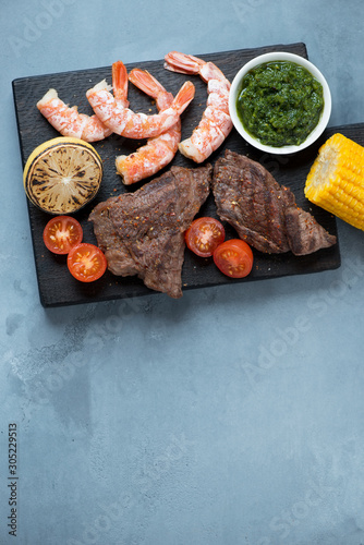 Black wooden serving board with surf and turf meal, top view on a grey concrete background with copyspace