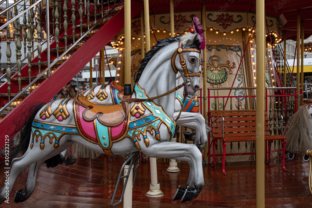 Merry go round. Fairytale painted white toy horse of vintage carousel in French style. Retro colorful illuminated merry-go-round with golden shiny lights. Kids playground at Christmas market in Europe
