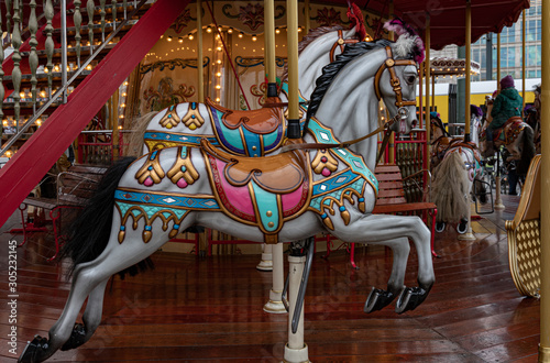 Carousel with horses. Ornate painted white toy horse of vintage carousel in French style. Retro colorful illuminated merry-go-round with golden shiny lights. Kids playground at Christmas funfair 