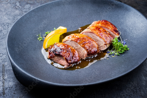 Traditional roasted Christmas duck breast with orange slice and herbs as closeup on a modern design plate photo