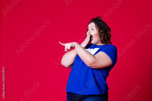 Surprised plus size model with wide open mouth in blue t-shirt on red background