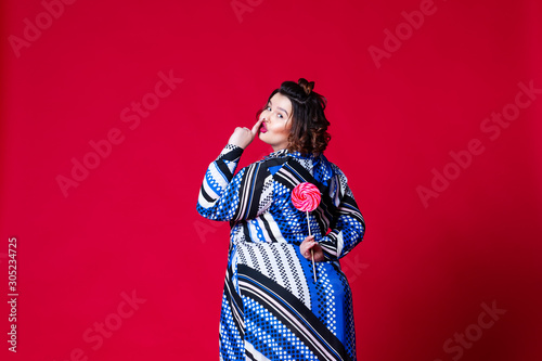 Plus size model in blue dress with big lollipop, fat woman on red background photo