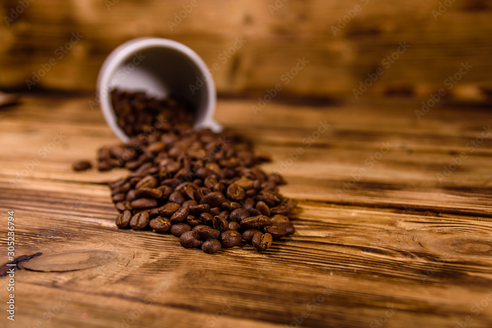 White cup and scattered coffee beans on wooden table White cup and scattered coffee beans on wooden table