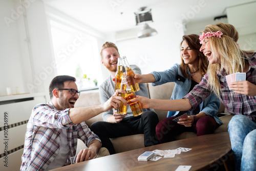 Group of happy friends playing cards and drinking