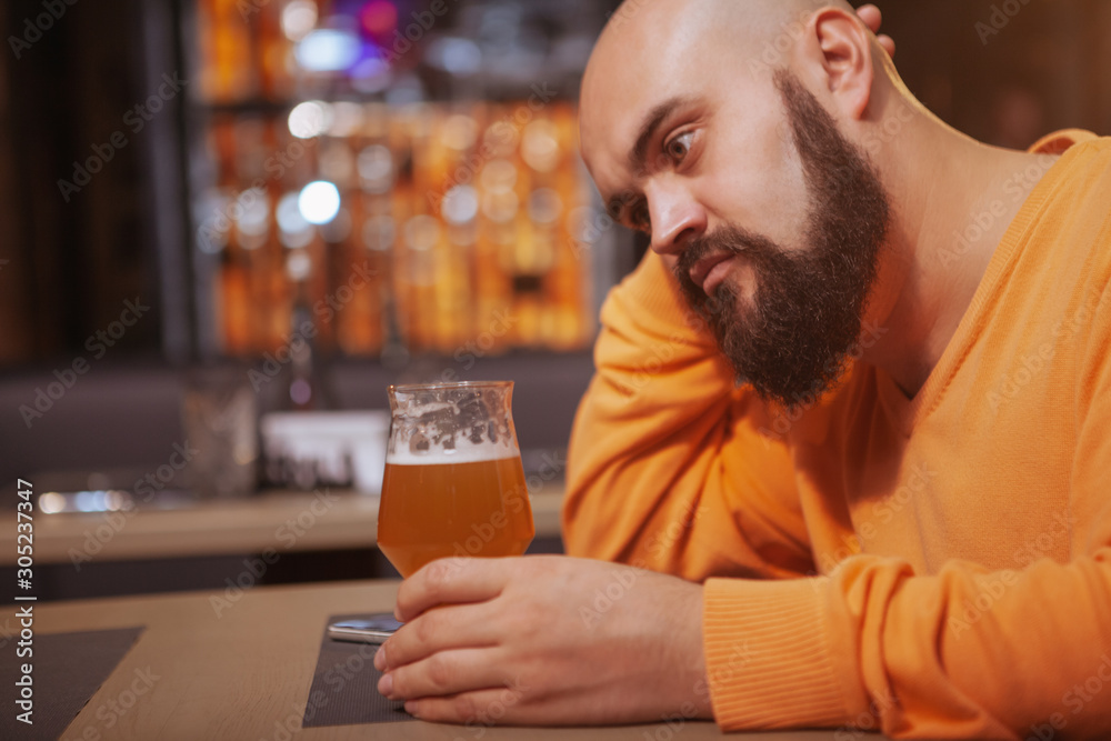 Depressed man drinking alone at the bar. Unhappy man holding a glass of beer at the pub