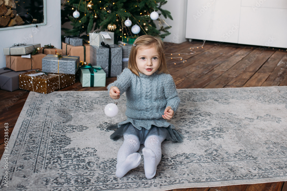 Naklejka premium Beautiful little girl playing with a Christmas decoration, Christmas tree on the background