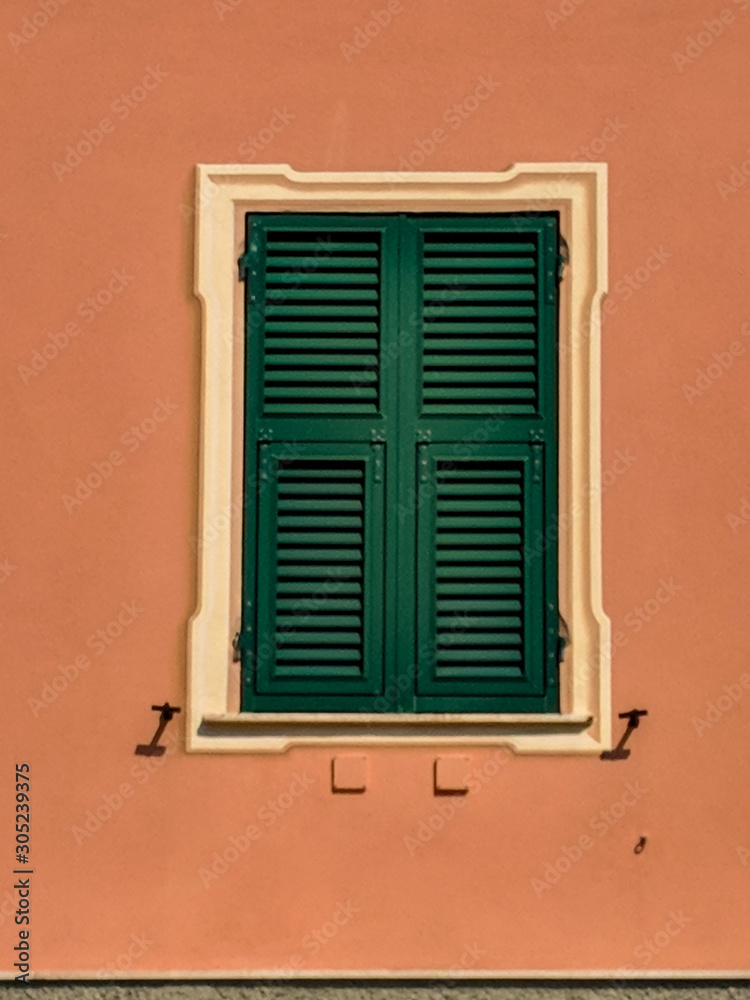 Closed window with green sun-blinds on an orange wall