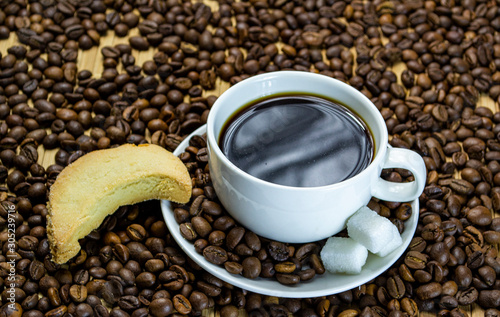 a cup of coffee with cookies, coffee grains scattered on a table near a cup with a coffee, selective focus