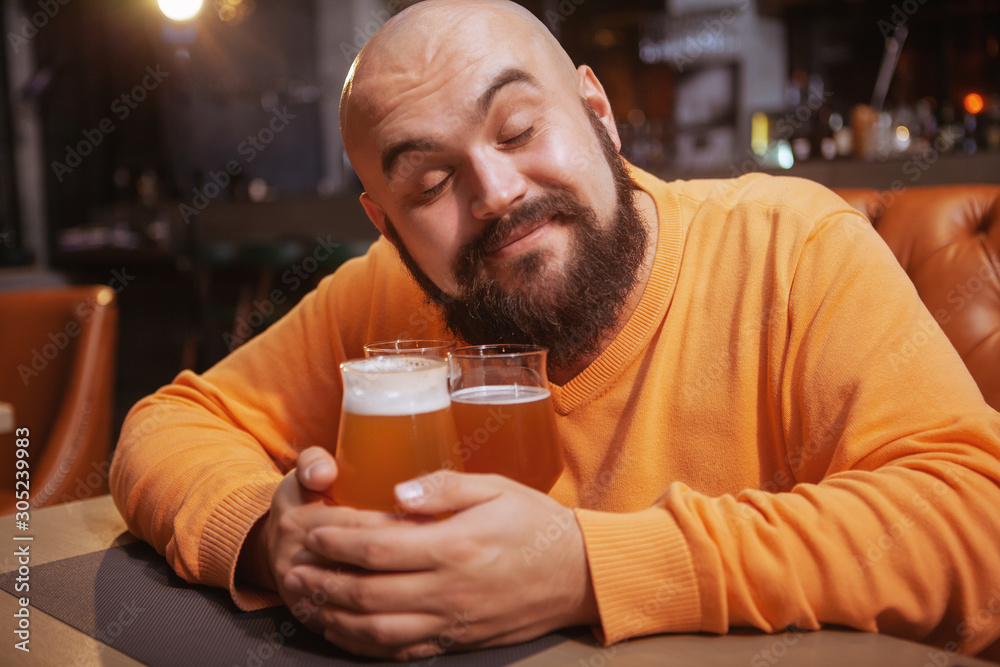Charming young man smiling with his eyec closed embracing beer mugs. Happy man hugging beer glasses Charming young man smiling with his eyec closed embracing beer mugs. Happy man hugging beer glasses