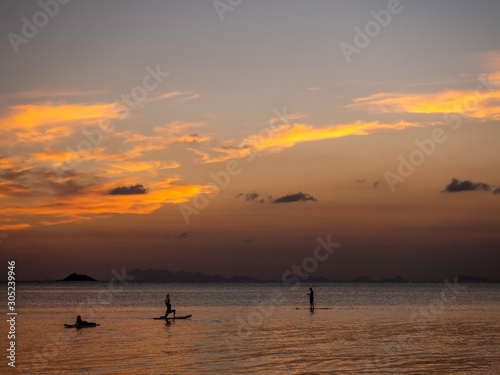 Silhouettes of people on sup boards in the rays of the setting sun against a background of clouds. Koh Phangan. Thailand.