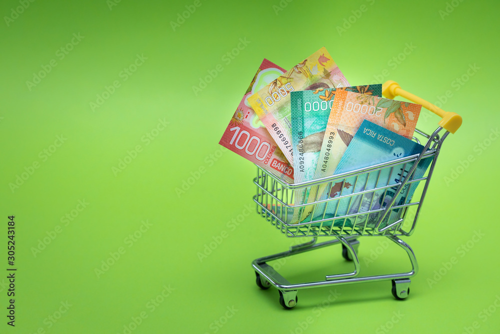 Miniature shopping trolley with Costa rican money. The concept of shopping and the power of the economy. Place for text