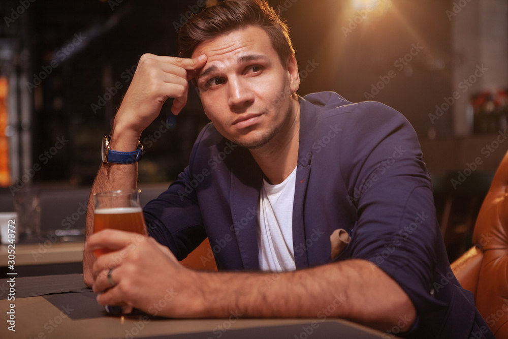 Handsome businessman drinking beer at the pub, looking away thoughtfully Handsome businessman drinking beer at the pub, looking away thoughtfully